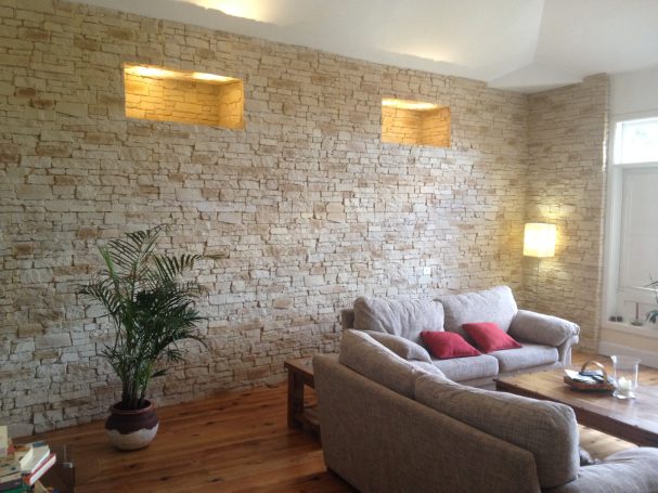 Paneles decorativos Sala de estar con pared de piedra, sofá gris y planta decorativa.