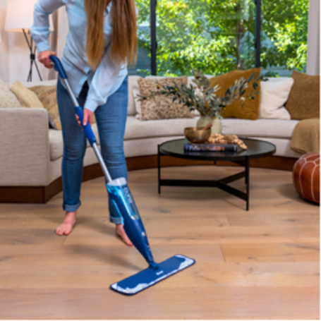 Limpieza y Mantenimiento Mujer limpia el suelo de madera con un mop con cabezal azul en una sala iluminada.