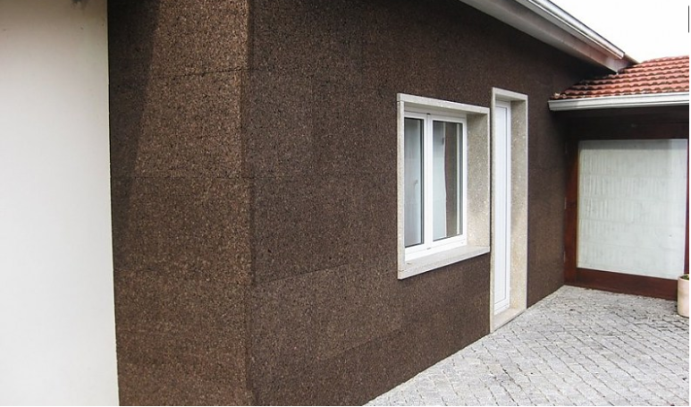 Aislante de Corcho Natural Fachada de casa con revestimiento marrón y ventanas blancas. Suelo de baldosas.